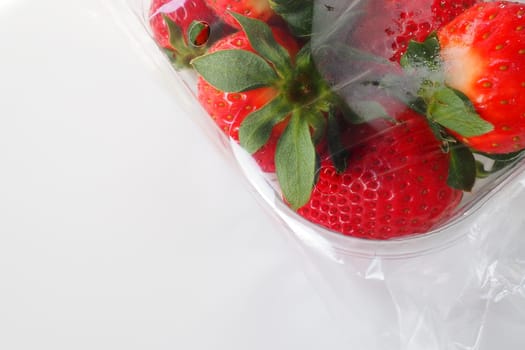 Ripe strawberries in a plastic package on a white background. Delicious fresh berries in a container for sale to customers. Keeping food fresh. Healthy food, vitamins and microelements