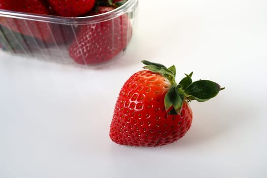 Ripe strawberries in a plastic package on a white background. Delicious fresh berries in a container for sale to customers. Keeping food fresh. Healthy food. One strawberry pulled out of the container