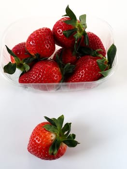 Ripe strawberries in a plastic package on a white background. Delicious fresh berries in a container for sale to customers. Keeping food fresh. Healthy food. One strawberry pulled out of the container