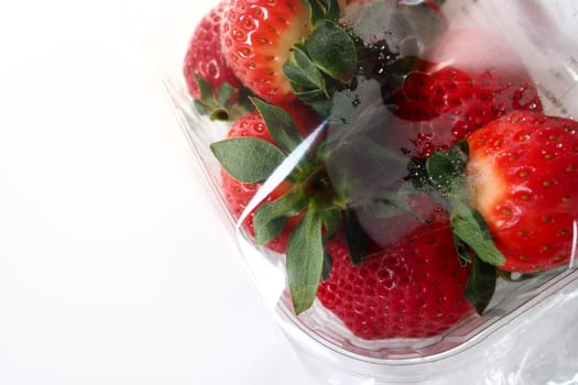 Ripe strawberries in a plastic package on a white background. Delicious fresh berries in a container for sale to customers. Keeping food fresh. Healthy food, vitamins and microelements