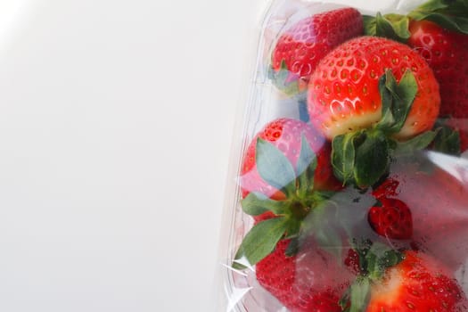 Ripe strawberries in a plastic package on a white background. Delicious fresh berries in a container for sale to customers. Keeping food fresh. Healthy food, vitamins and microelements