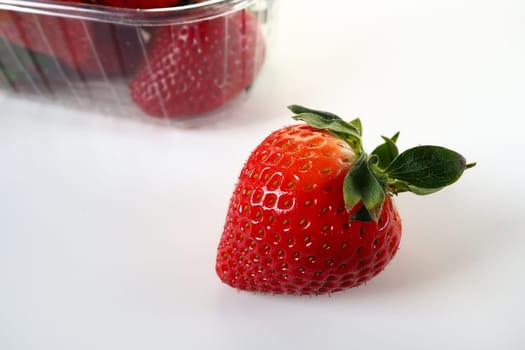 Ripe strawberries in a plastic package on a white background. Delicious fresh berries in a container for sale to customers. Keeping food fresh. Healthy food. One strawberry pulled out of the container