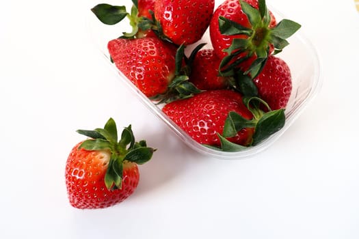 Ripe strawberries in a plastic package on a white background. Delicious fresh berries in a container for sale to customers. Keeping food fresh. Healthy food. One strawberry pulled out of the container