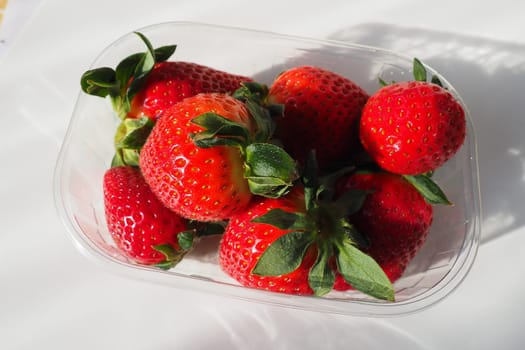 Ripe strawberries in a plastic package on a white background. Delicious fresh berries in a container for sale to customers. Keeping food fresh. Healthy food, vitamins and microelements