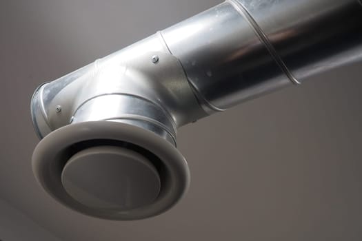 Extractor hood in a public toilet. Round metal pipe with gray air extractor. Engineering ventilation systems. Galvanized pipes under the ceiling of the room. Plastic round tip.