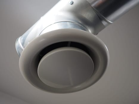 Extractor hood in a public toilet. Round metal pipe with gray air extractor. Engineering ventilation systems. Galvanized pipes under the ceiling of the room. Plastic round tip.