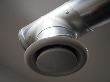 Extractor hood in a public toilet. Round metal pipe with gray air extractor. Engineering ventilation systems. Galvanized pipes under the ceiling of the room. Plastic round tip.