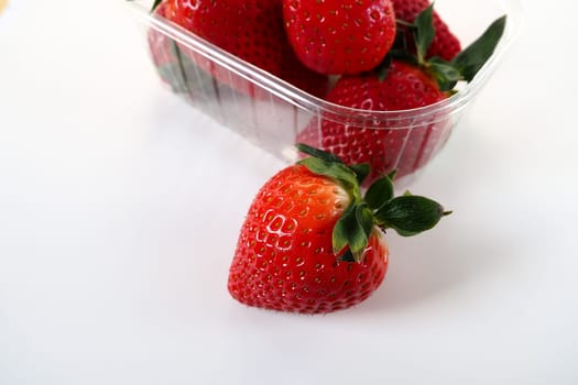 Ripe strawberries in a plastic package on a white background. Delicious fresh berries in a container for sale to customers. Keeping food fresh. Healthy food. One strawberry pulled out of the container