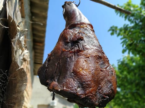 Homemade ham. Farm product of Serbian producers. Dried salted smoky pork hind leg. Meat delicacy. Meat suspended in the air to dry. Protein diet. Traditional cooking.