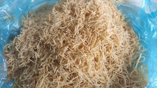 Thin dry vermicelli. Wheat flour product containing gluten, vitamins, carbohydrates, proteins and fats. Small pasta in a blue plastic bag. Fast food.