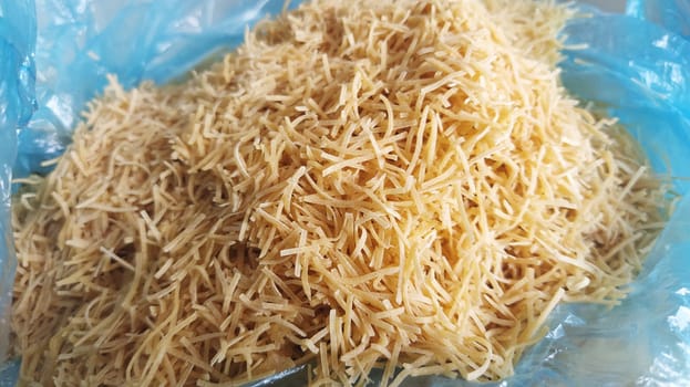 Thin dry vermicelli. Wheat flour product containing gluten, vitamins, carbohydrates, proteins and fats. Small pasta in a blue plastic bag. Fast food.