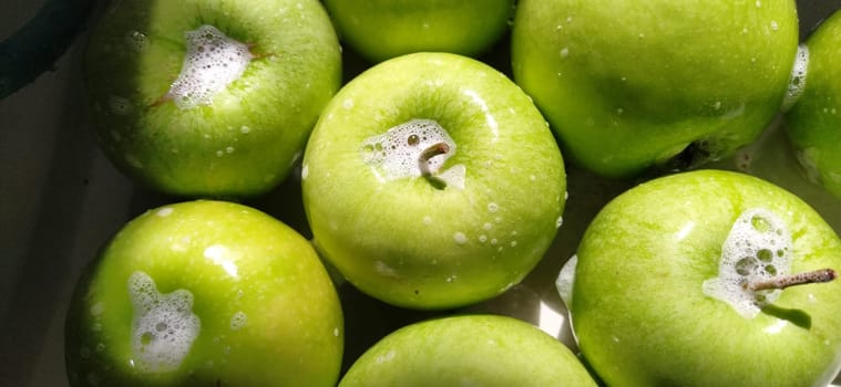 Wet soapy green apples. Thoroughly wash vegetables and fruits with water and soap. Prevention of infectious diseases. Apples close up. Vegetarianism. High glycemic index. Soapy foam sparkles in sunlight.