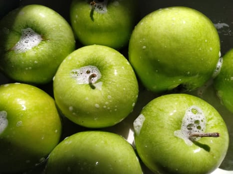 Wet soapy green apples. Thoroughly wash vegetables and fruits with water and soap. Prevention of infectious diseases. Apples close up. Vegetarianism. High glycemic index. Soapy foam sparkles in sunlight.