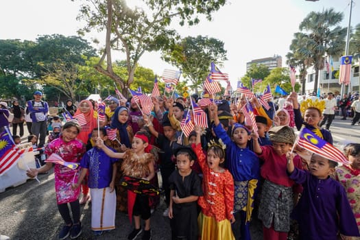 George Town, Penang, Malaysia - Aug 31 2022: Group of children wear traditional costume raise the Malaysia flag during celebration Independence day