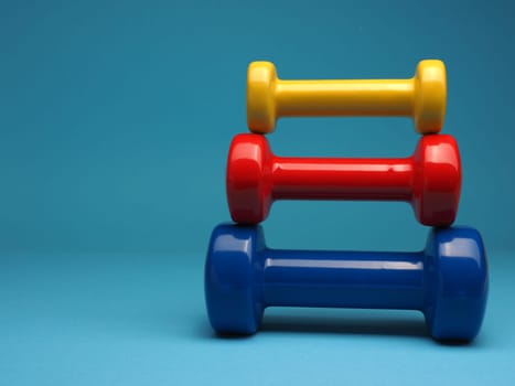 Red, blue and yellow dumbbells on a blue background, space for your text, fitness or diet concept