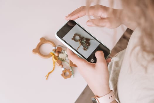 Baby natural safe accessories with beads, eco style. Zero waste. Eco teether toy, pacifier with trinket rattle decoration. Cropped woman taking photo item for shop inventory. Online marketplace