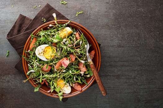 Dandelion salad with eggs and roasted bacon on grey background