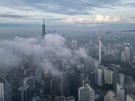 Bukit Bintang, Kuala Lumpur, Malaysia - Nov 13 2022: The tall spire of the Merdeka 118 and KL Tower pierces through the low clouds, creating a surreal view.