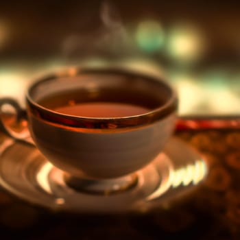 Cup of a hot tea in cafe. Anamorphic bokeh effect. Tilt-shift photo. Tasty aromatic tea in a lovely cup with a saucer. The tea is getting cold. Natural aroma. Label or advertisement. Evaporation