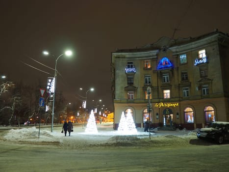 Petrozavodsk, Karelia, Russia, January 01, 2021. Karl Marx Avenue, Cafe Parisianka in the evening in winter. Snow drifts, Christmas street lights and decorations. People walk along the street
