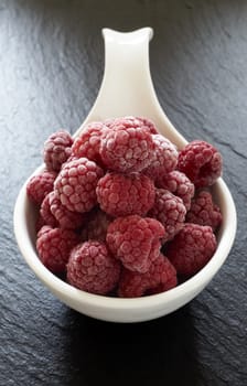 Frozen raspberries in porcelain bowl on slate plate