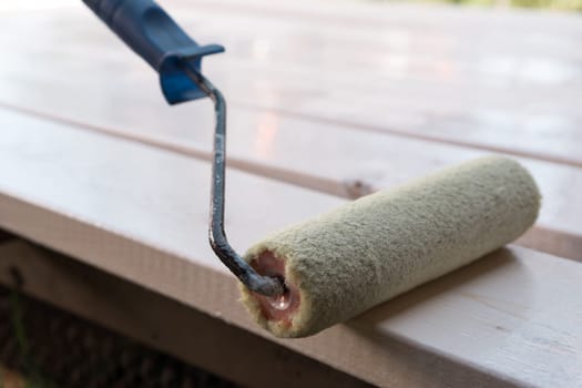 Close up white soft professional paint roller applicator with handle lying on wooden board. Brushing, coloring and making cosmetic repairment. Renewal work, stucco and repair. House remodeling
