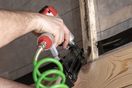 Cropped man hands working with stapler, nail gun with green cable and wooden board. Clipping and scoring metal staples, making layout on wooden plank. Builder occupation, civil engineer. Low angle