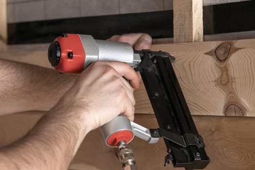 Close up cropped male hands using pneumatic nailer, stapler nail gun for wooden planks and board. Clipping and scoring metal nails and staples, making layout on wooden plank. Builder first person view