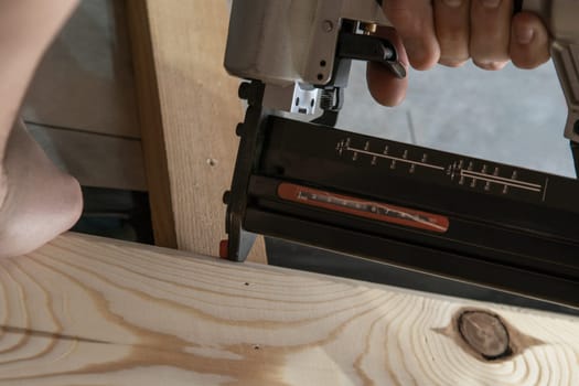 Cropped man hands using pneumatic construction stapler, pistol nail gun for wooden plank. Clipping, scoring metal nails and staples. Hammer replacement, new technology. Builder occupation, diy