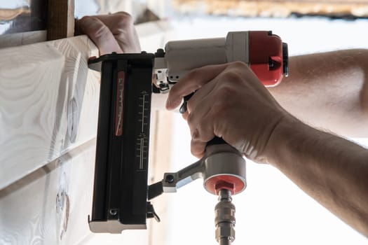 Cropped male builder hands use pneumatic stapler gun for clipping wooden timber board. Scoring metal nails and staples, making layout on wooden plank. Builder and civil engineer occupation. Side view