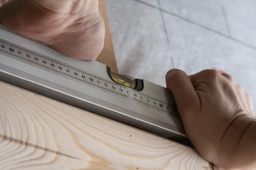 Close up cropped male worker hands hold water pass level for building wooden structure. Renovation and repair of houses. Measuring and fixing level, builder equipment for carpenters. Low angle view