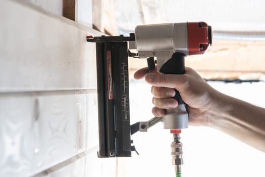 Unrecognizable builder worker hand using pneumatic stapler for wooden board. Clipping metal nails and staples, making layout on wooden plank frame. Builder occupation, civil engineer. Side view