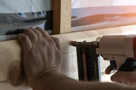 Cropped builder hands holding pneumatic nail gun, stapler for wooden board. Scoring and setting up metal staples, making layout on wooden plank. Handyman work, do it yourself. Builder occupation