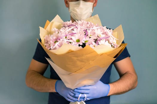 courier in medical gloves and a mask delivers a bouquet of chrysanthemums. Contactless flower delivery during quarantine due to the coronavirus epidemic
