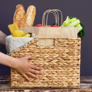 Fresh eco organic vegetables, greens and fruits, cereals and pasta in a wicker basket in the hands of a child. Delivery or donation of ecological farm food concept
