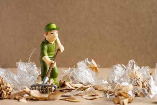 A toy man in a worker's suit rakes a large amount of garbage. Environmental protection and ecology concept