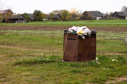Overflowing rusty trash can in the countryside. Rubbish scattered on the ground. Environmental protection problem