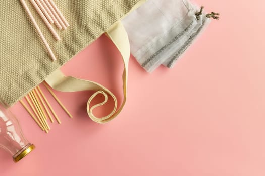 Fabric cotton shopping bags, glass bottles and jars, paper straws and wooden sticks on a pink background. Zero waste and ecological concept. Top view. Copy space.