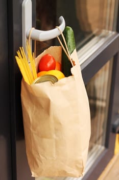 A paper bag with food from delivery on the handle of the front door. Contactless delivery. Donation during coronavirus. Volunteering and delivery during quarantine concept.