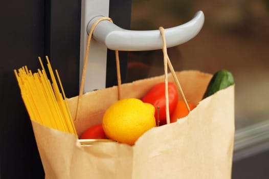 A paper bag with food from delivery on the handle of the front door, closeup. Contactless delivery. Donation during coronavirus. Volunteering and delivery during quarantine concept.