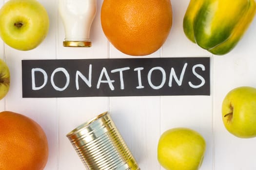 Cereals, canned food, milk, vegetables and fruits with a chalk Donations sign on a white wooden table. Flat lay. Charity and donation concept.