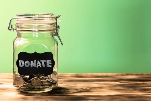 Glass jar with coins with chalk tag Donate on a green background, donation and charity concept. Copy space.