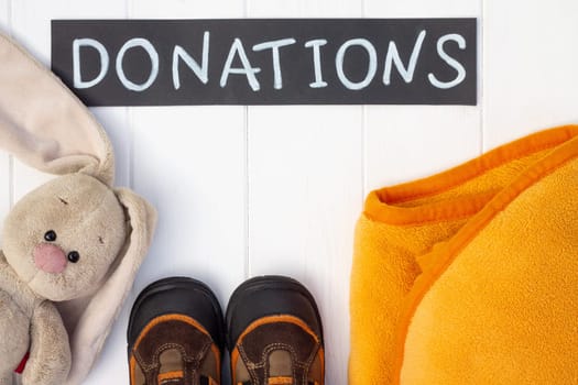 Children's plaid and boots with a chalk Donations sign on a white wooden table. Flat lay. Charity and donation concept.