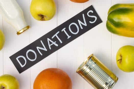 Cereals, canned food, milk, vegetables and fruits with a chalk Donations sign on a white wooden table. Flat lay. Charity and donation concept.