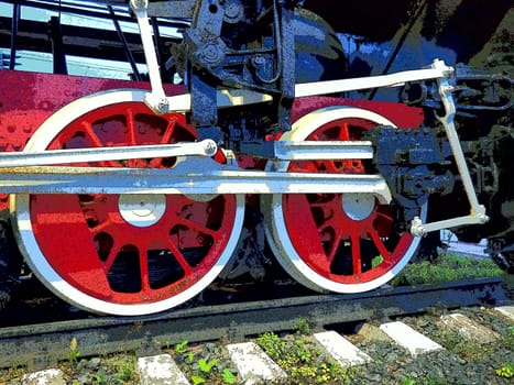 Retro vintage wheels of a locomotive or train close up. Red large heavy metal wheels with piston guiding mechanisms. Locomotive of the 19th - 20th centuries with a steam engine. Bright vivid photo.
