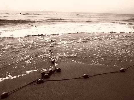 Buoys on a rope near sea water. The buoys are bright pink restraints to alert people to the depth of the water. Sepia. Delimiting a place on a sandy beach between hotels. Waves with bubbles.