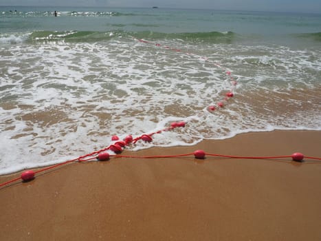 Buoys on a rope in sea water. The lifebuoys are pink restraints to alert people to the depth of the water. Rescue of the drowning. Delimiting a place on a sandy beach between hotels. Wave with bubbles.