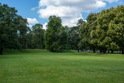 Long barrow mound and tall trees by the exterior of the Great Circle mound at the Newark Earthworks built by prehistoric indigenous people in Ohio. Green grass, sunny outdoors with no people and copy space.
