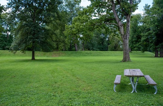 An empty picnic table by the exterior of the Great Circle at the Newark Earthworks built by prehistoric indigenous people in Ohio. Green grass, sunny outdoors with no people and copy space.