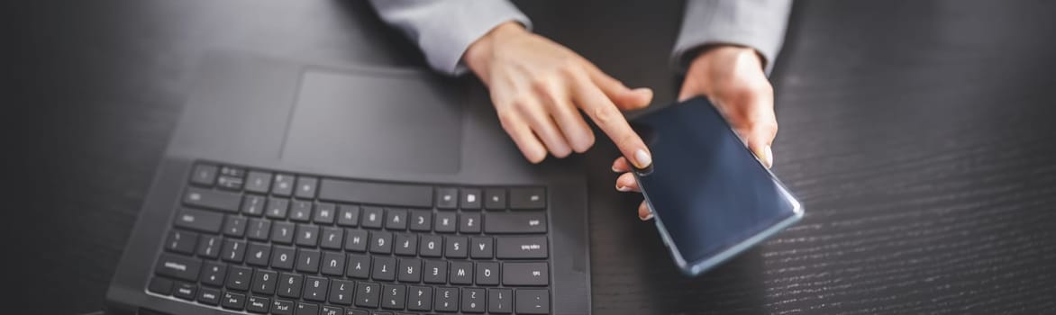 Woman holding in her hands mobile phone and typing on the laptop. Concept of the e-commerce, business and surfering in network.